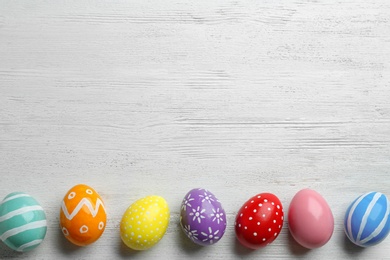 Photo of Flat lay composition of painted Easter eggs on wooden table, space for text