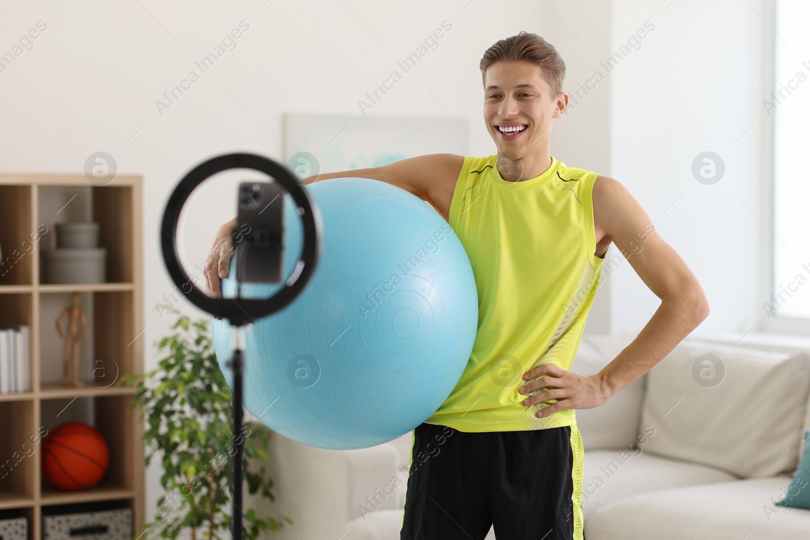 Photo of Smiling sports blogger holding fit ball while streaming online fitness lesson at home