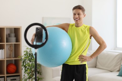 Photo of Smiling sports blogger holding fit ball while streaming online fitness lesson at home