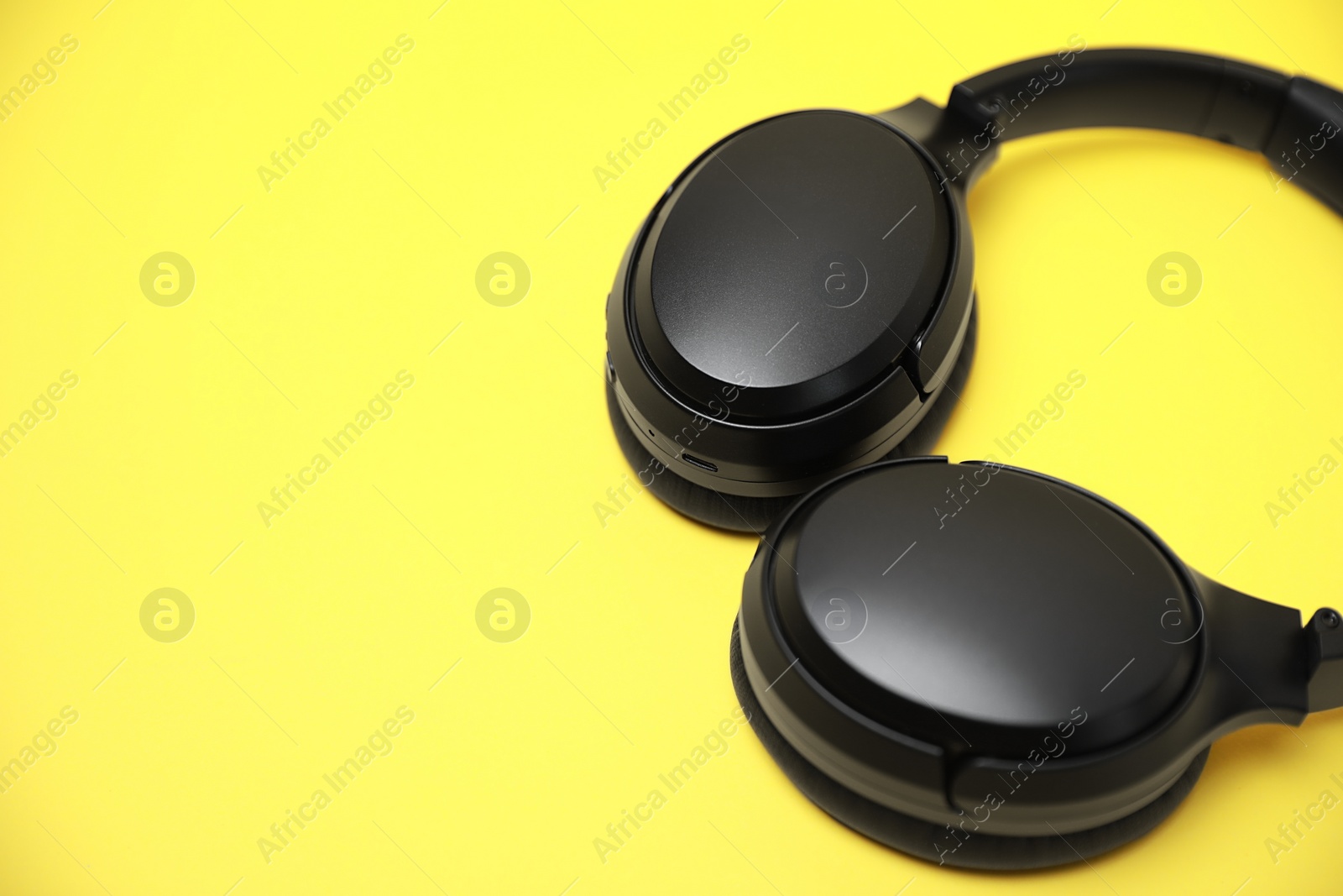 Photo of Modern wireless headphones on yellow background, closeup. Space for text