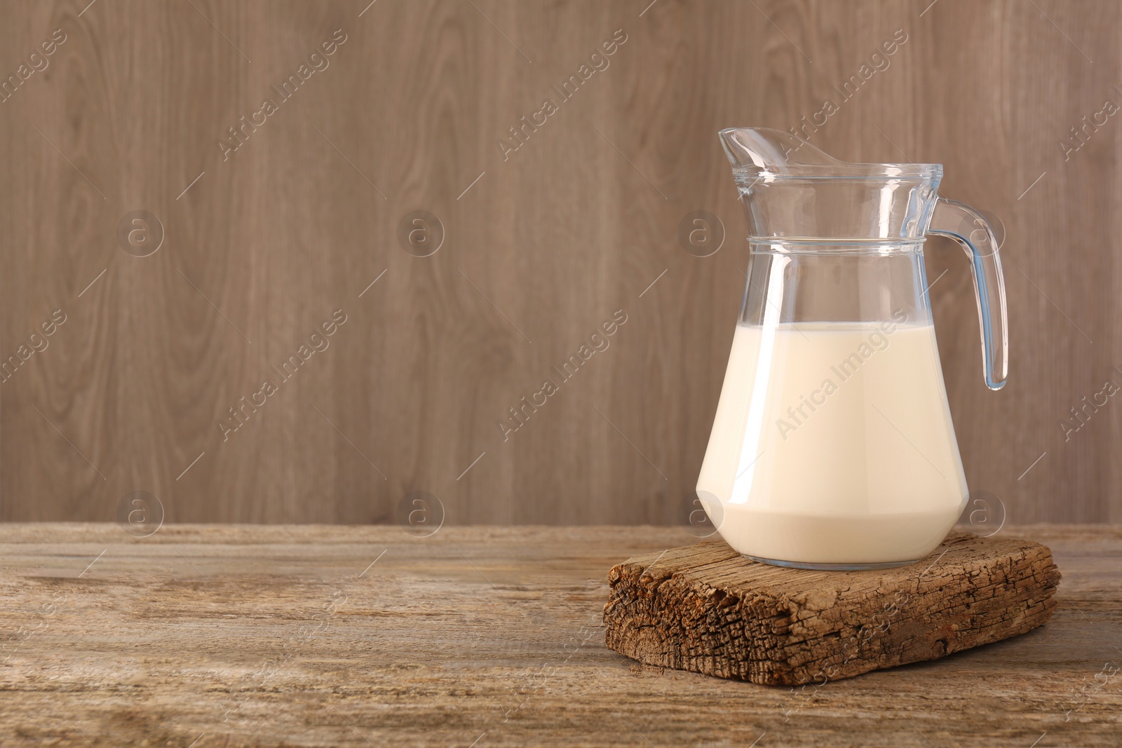 Photo of Jug of fresh milk on wooden table, space for text