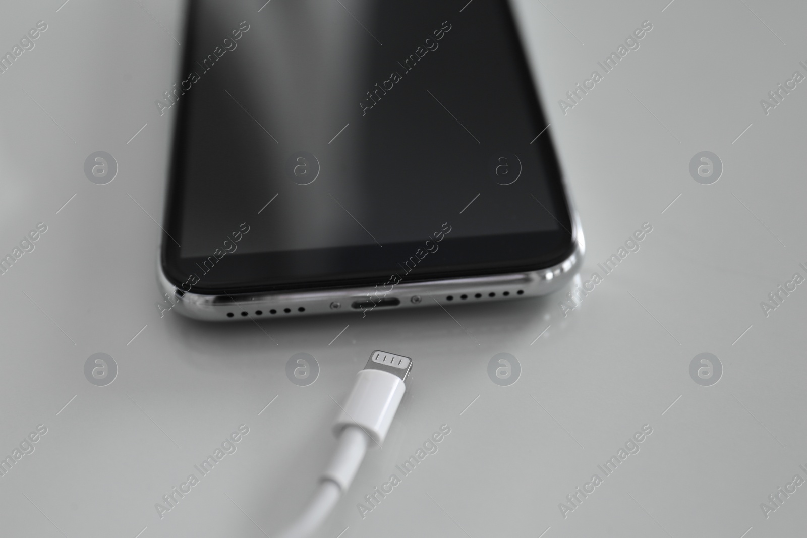 Photo of Mobile phone and charging cable on white table, closeup