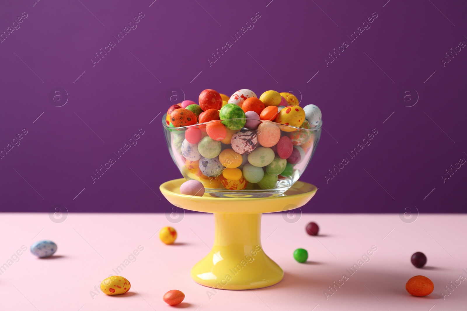 Photo of Delicious colorful dragee candies on pink table against purple background