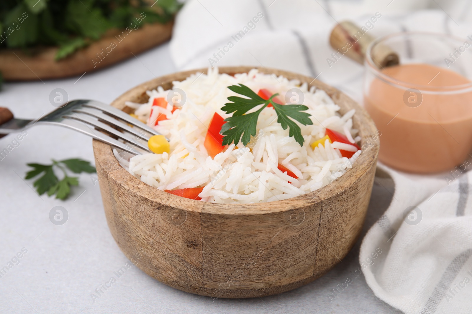 Photo of Bowl of delicious rice with vegetables and parsley served on light gray table, closeup