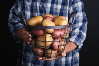 Photo of Person holding basket with fresh organic potatoes on black background