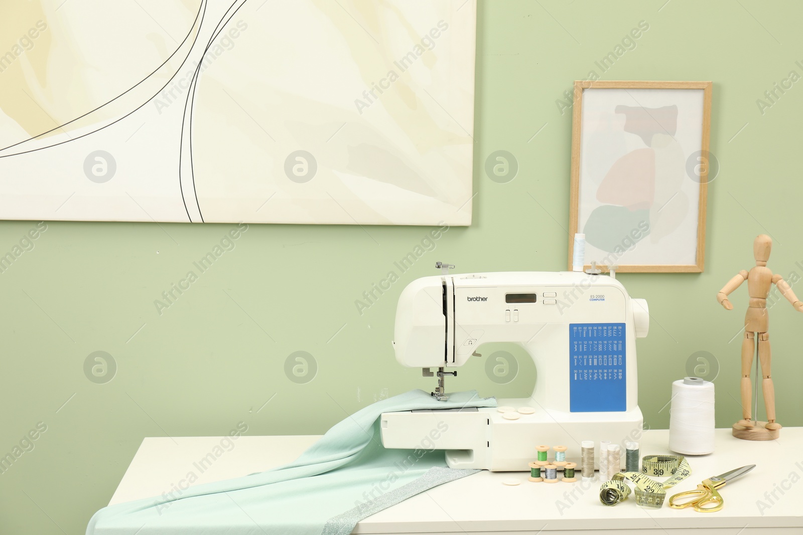 Photo of Modern sewing machine with cloth and craft accessories on white table near light green wall