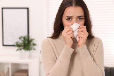 Photo of Sick woman with tissue blowing nose at home, space for text. Cold symptoms