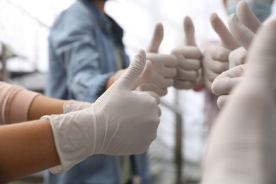 Group of people in white medical gloves showing thumbs up on blurred background, closeup