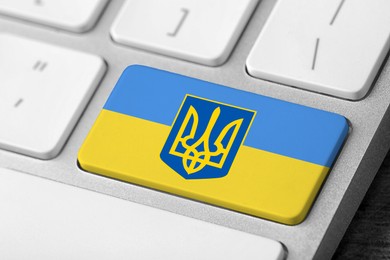 Button in colors of Ukrainian flag with coat of arms on keyboard, closeup view