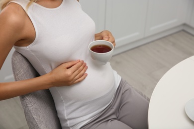 Photo of Beautiful pregnant woman drinking tea in kitchen, closeup