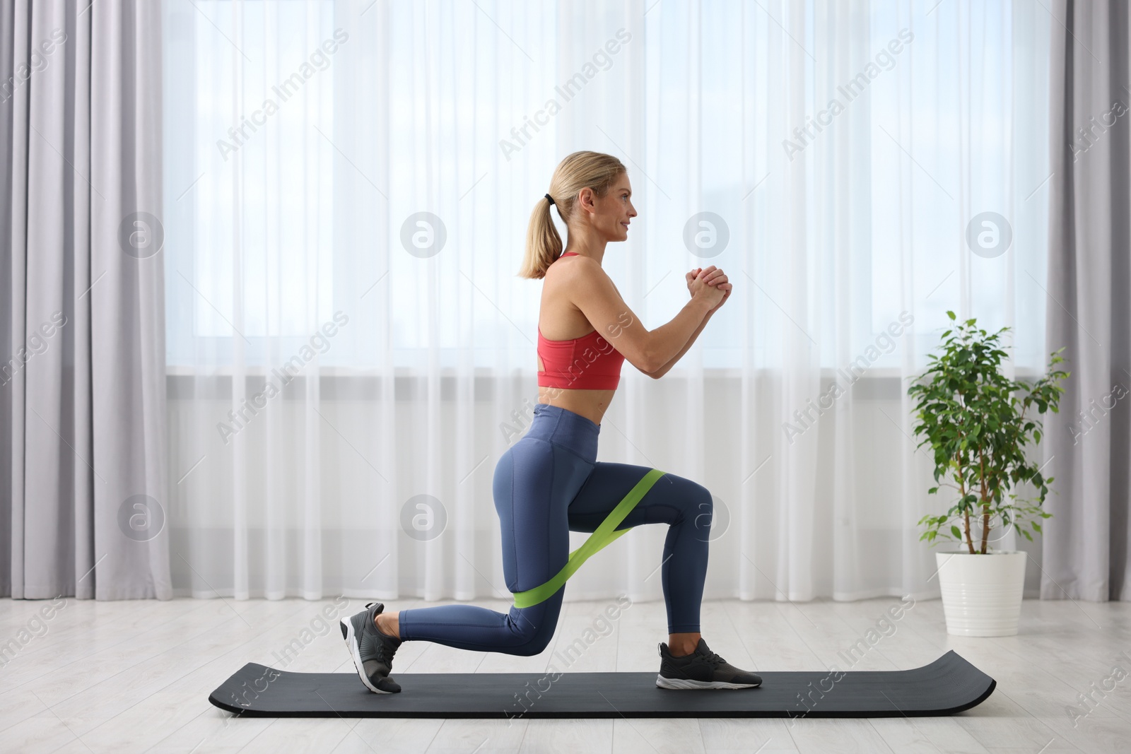 Photo of Athletic woman doing exercise with fitness elastic band on mat at home