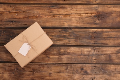 Photo of Parcel with tag and space for text on wooden background, top view