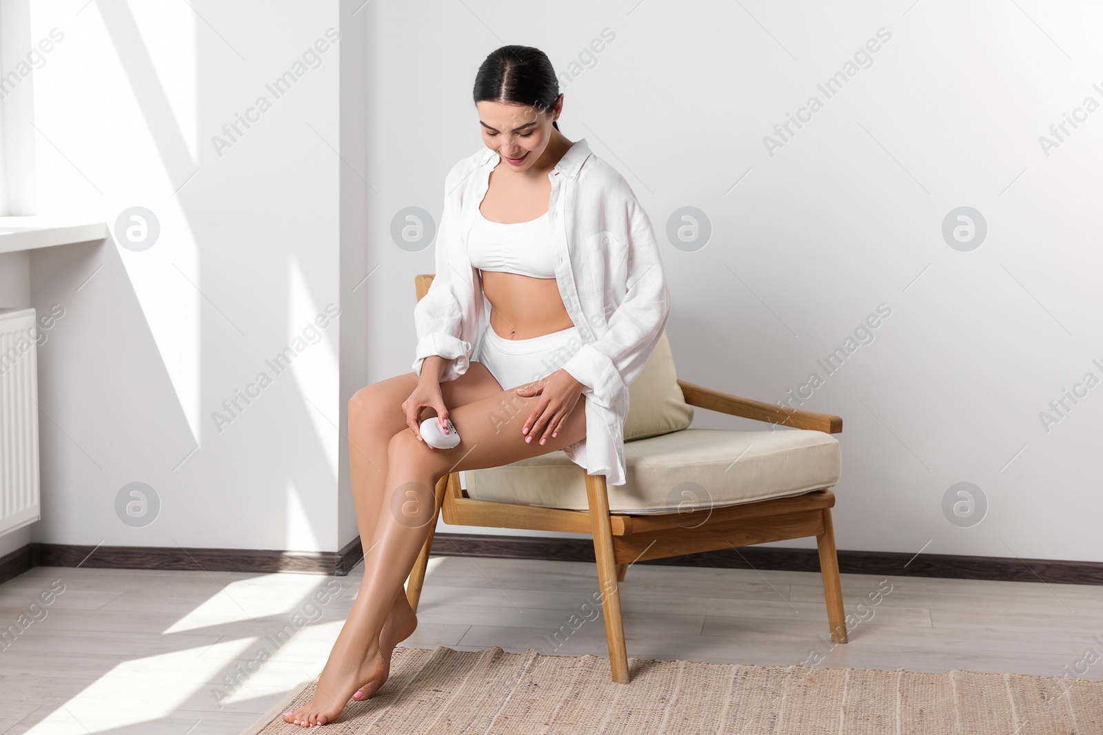 Photo of Young woman epilating her legs in room