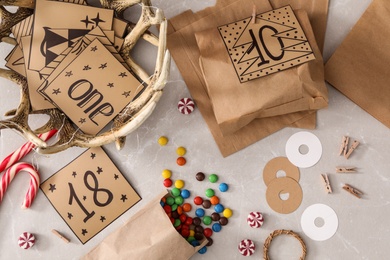 Photo of Flat lay composition with paper bags and treats on grey marble table. Creating advent calendar