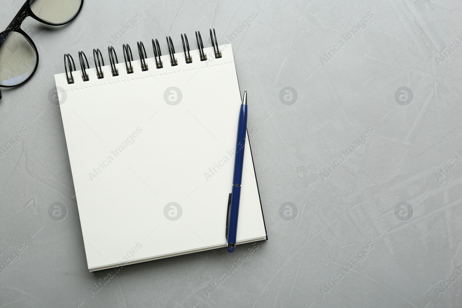 Photo of Notebook, glasses and pen on light textured table, flat lay. Space for text