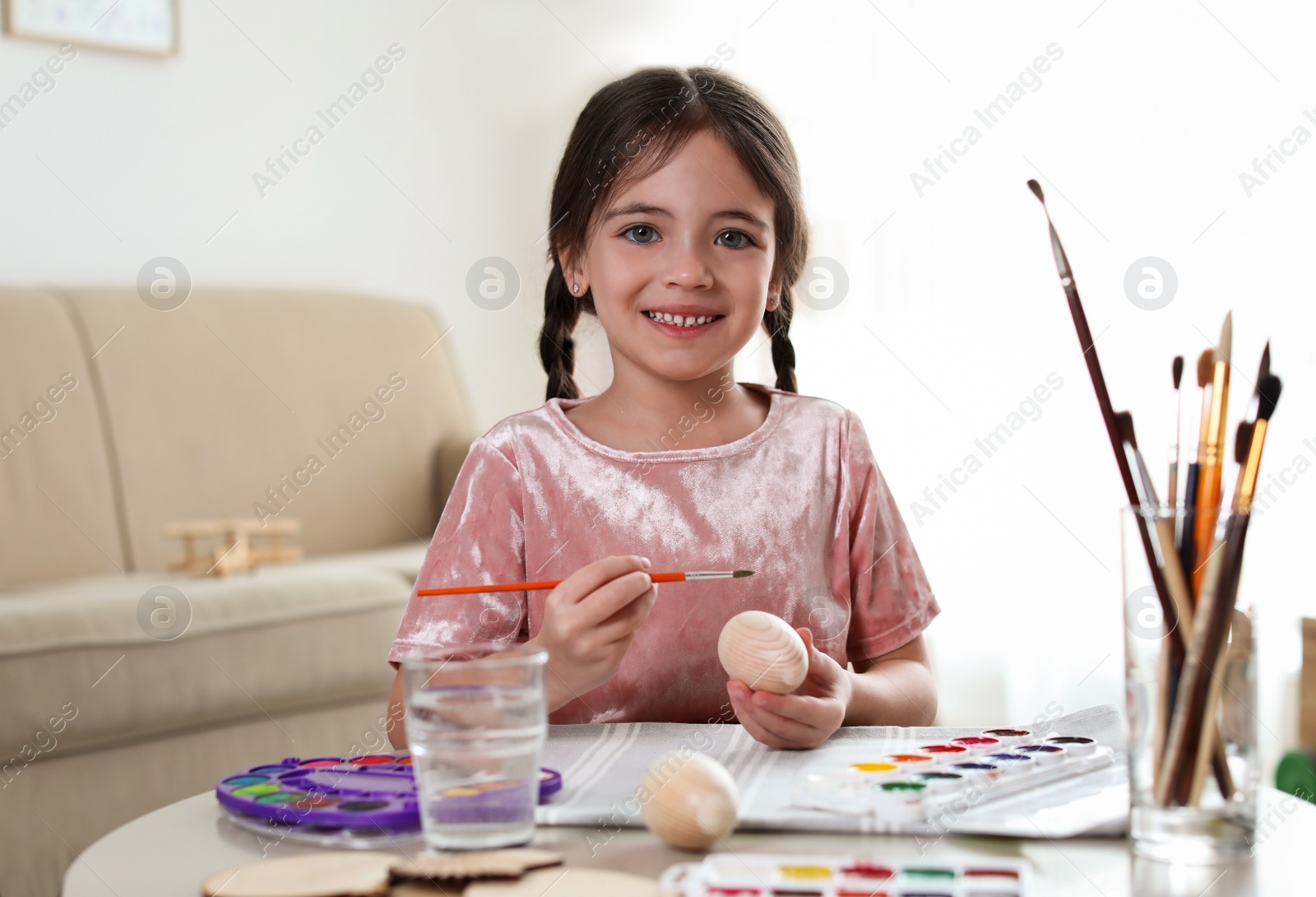 Photo of Little girl painting decorative egg at table indoors. Creative hobby