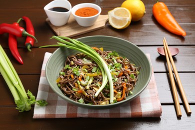 Photo of Stir-fry. Delicious cooked noodles with chicken and vegetables in bowl on wooden table