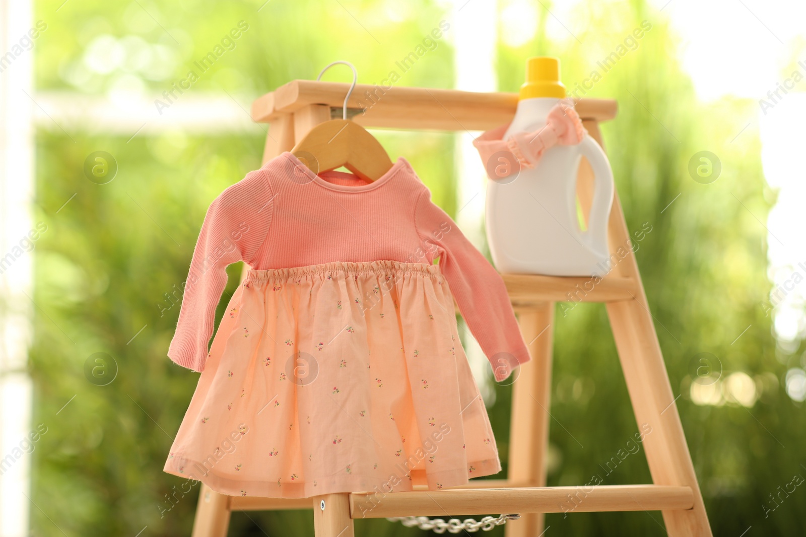 Photo of Bottle of detergent and children's clothes on wooden ladder outdoors