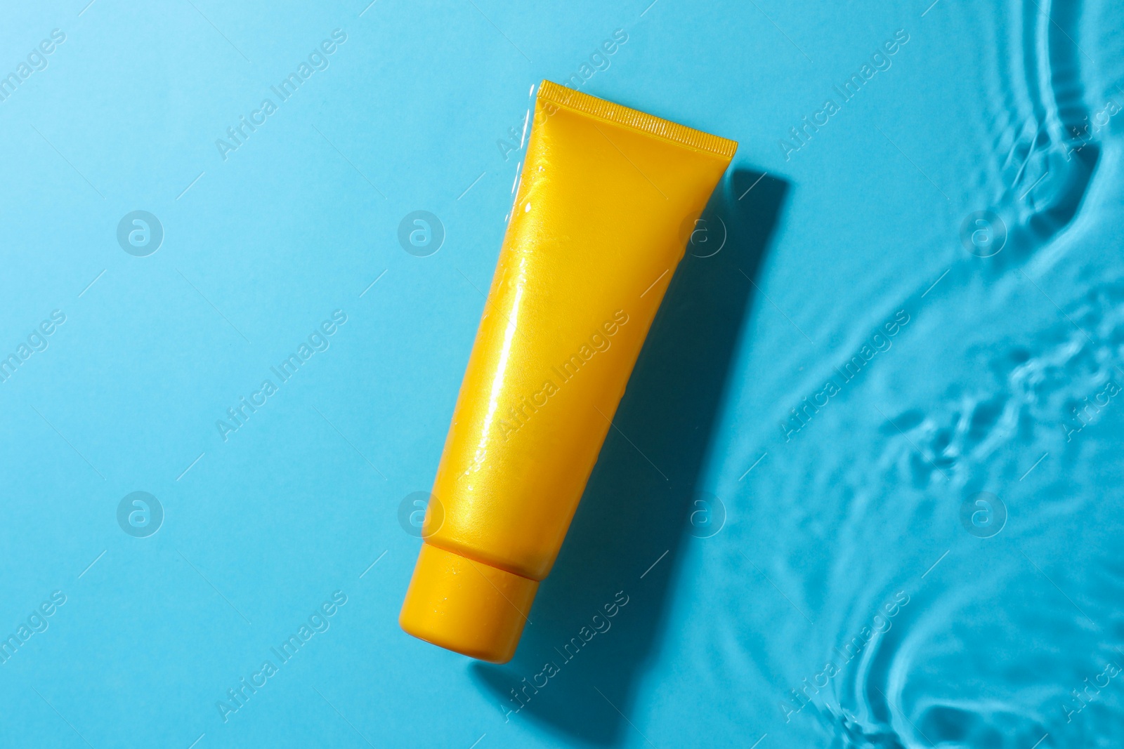 Photo of Tube with moisturizing cream in water on light blue background, top view