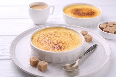 Photo of Delicious creme brulee in bowls, vanilla pods, sugar cubes and coffee on white wooden table, closeup