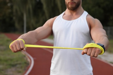 Photo of Muscular man doing exercise with elastic resistance band at stadium, closeup
