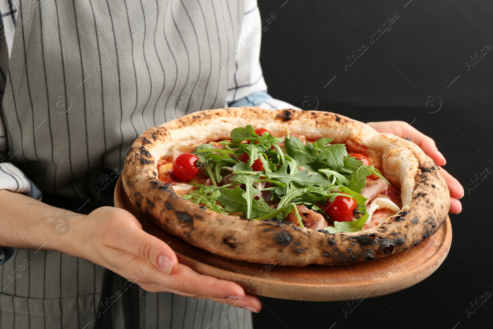 Photo of Woman holding tasty pizza with meat and arugula on black background, closeup