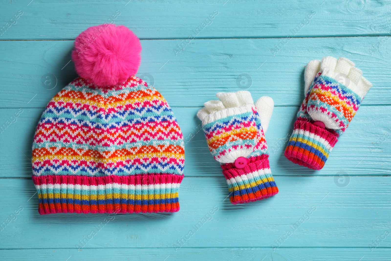 Photo of Warm knitted hat and mittens on blue wooden background, flat lay