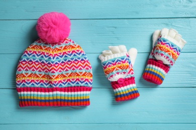 Warm knitted hat and mittens on blue wooden background, flat lay