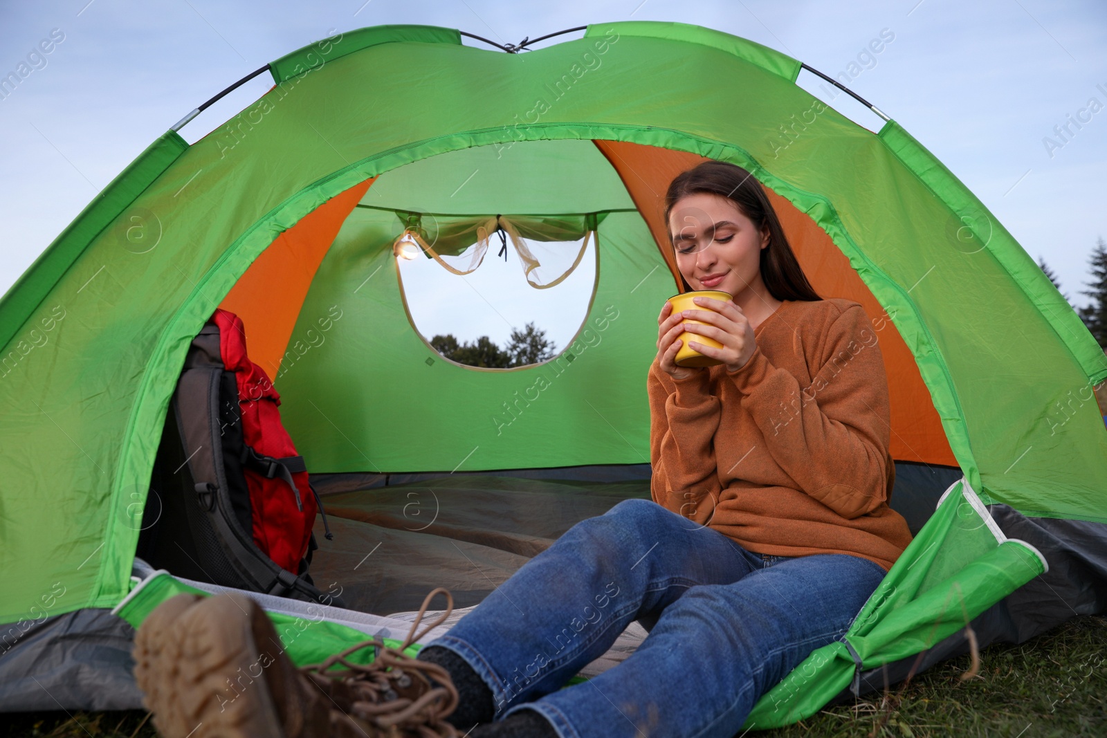 Photo of Young woman with cup of drink in camping tent outdoors