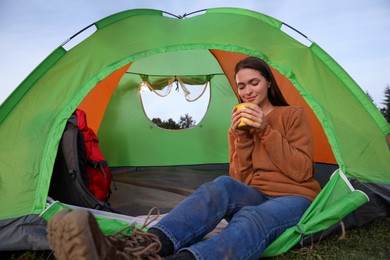 Photo of Young woman with cup of drink in camping tent outdoors