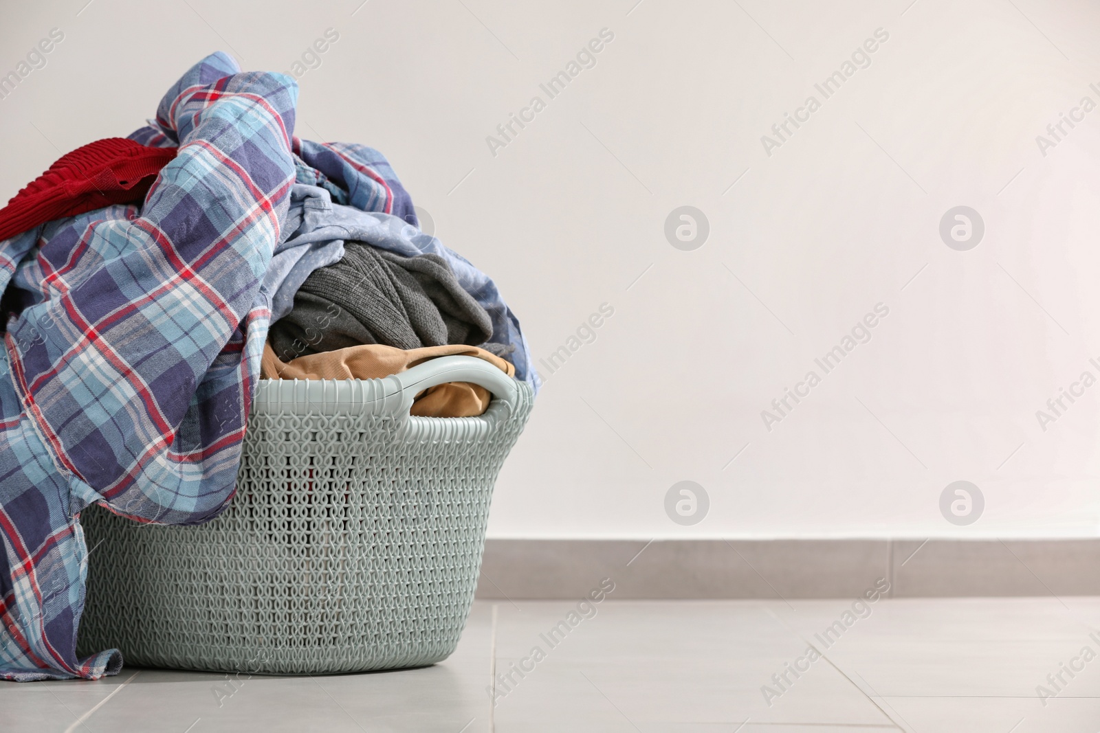 Photo of Laundry basket with clothes near white wall. Space for text