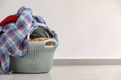 Photo of Laundry basket with clothes near white wall. Space for text