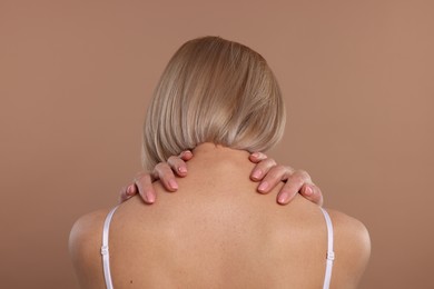 Photo of Woman suffering from pain in her neck on beige background, back view