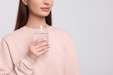 Photo of Healthy habit. Woman holding glass with fresh water on light grey background, closeup. Space for text