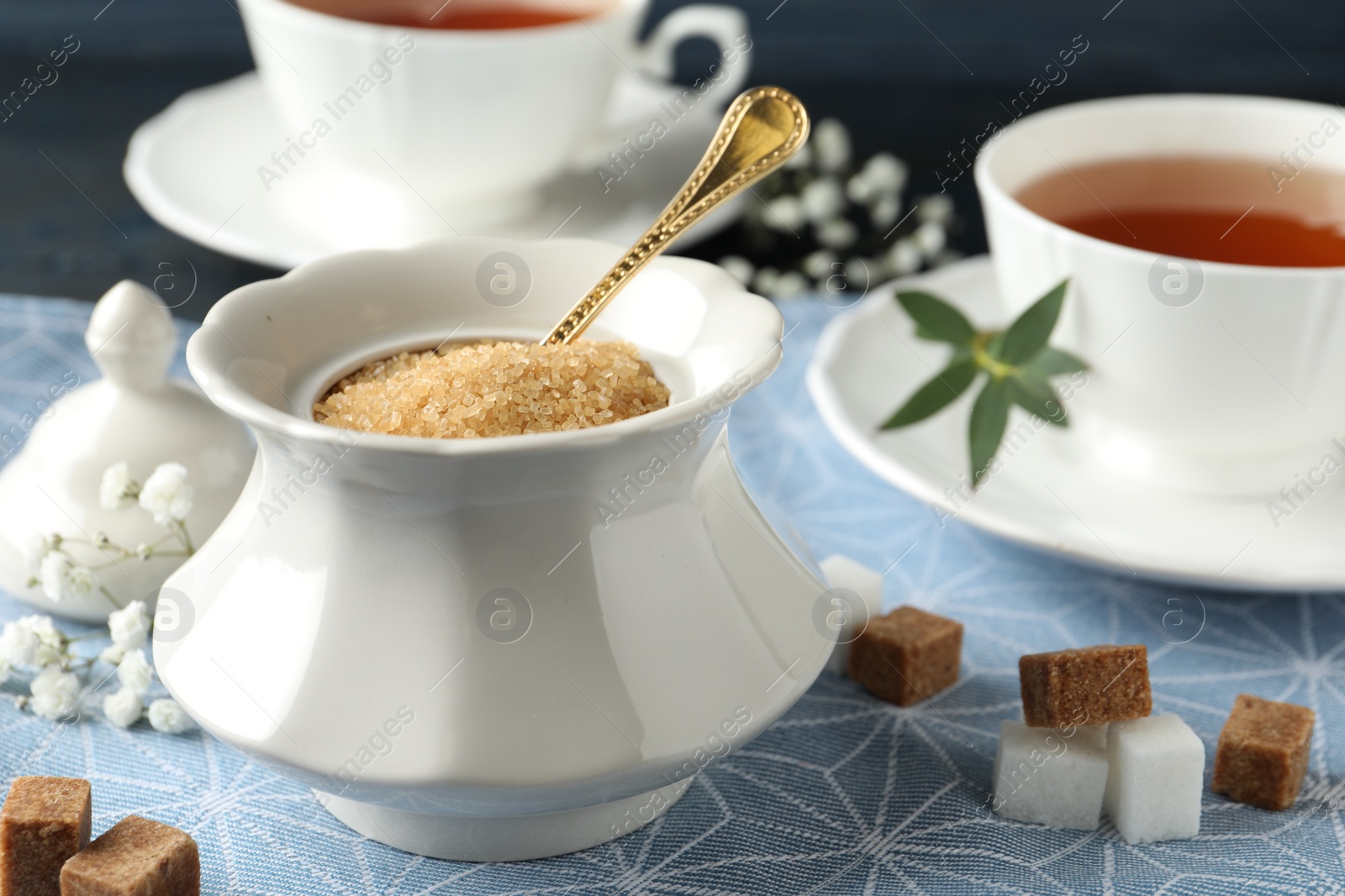 Photo of Ceramic bowl with brown sugar and cups of tea on table