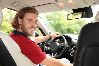 Photo of Attractive young man driving his luxury car, view from backseat