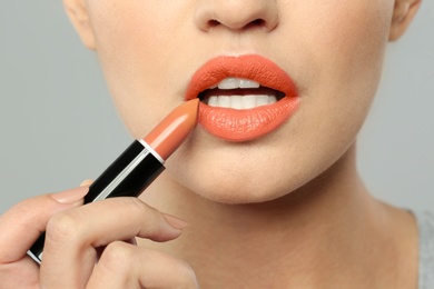 Young woman applying beautiful lipstick on gray background, closeup