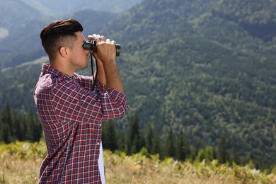 Man looking through binoculars in mountains on sunny day