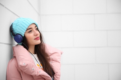 Photo of Beautiful young woman listening to music with headphones near light wall. Space for text