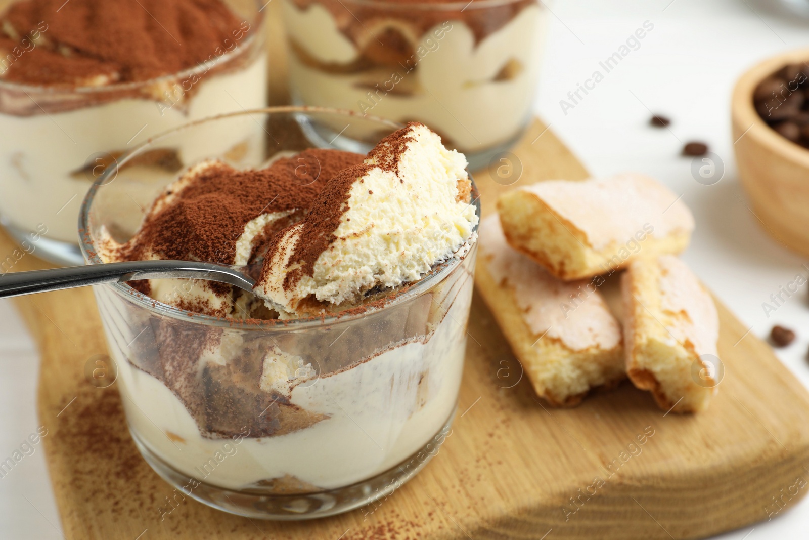 Photo of Delicious tiramisu in glasses, cookies and spoon on white table, closeup