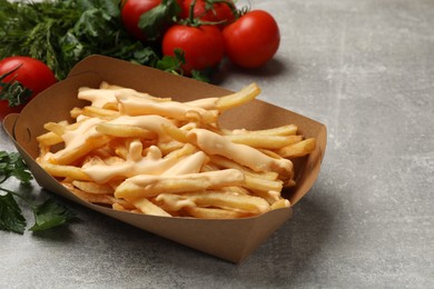 Photo of Tasty potato fries, cheese sauce in paper container and products on grey table, closeup