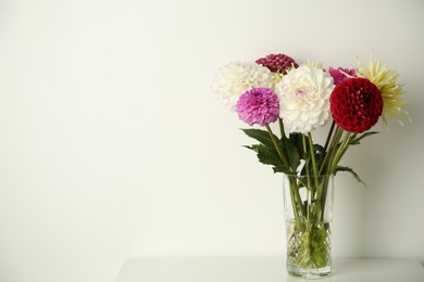 Photo of Bouquet of beautiful Dahlia flowers in vase on white table. Space for text