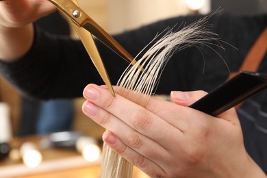 Hairdresser cutting client's hair with scissors in salon, closeup