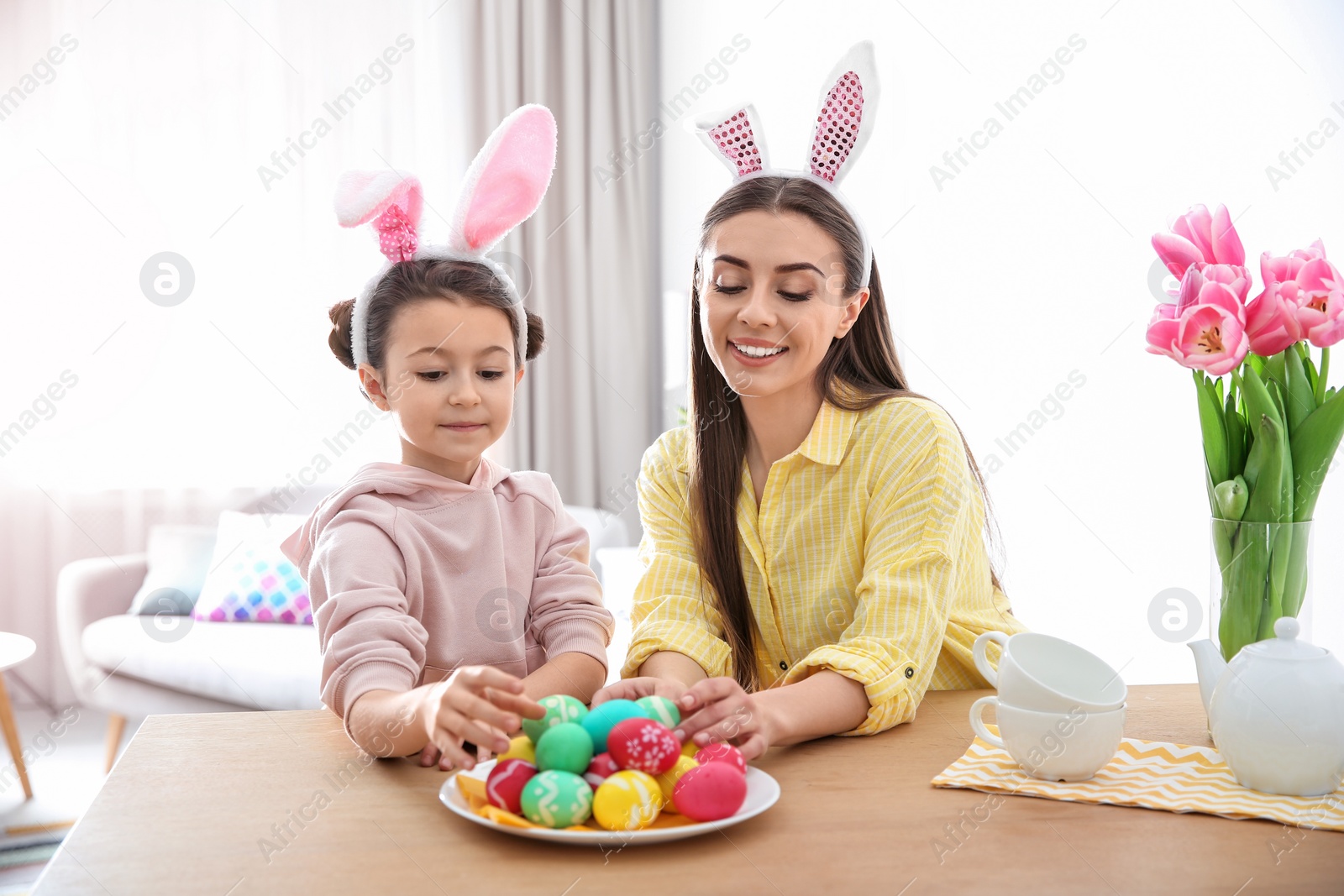 Photo of Mother and daughter with bunny ears headbands and painted Easter eggs at home