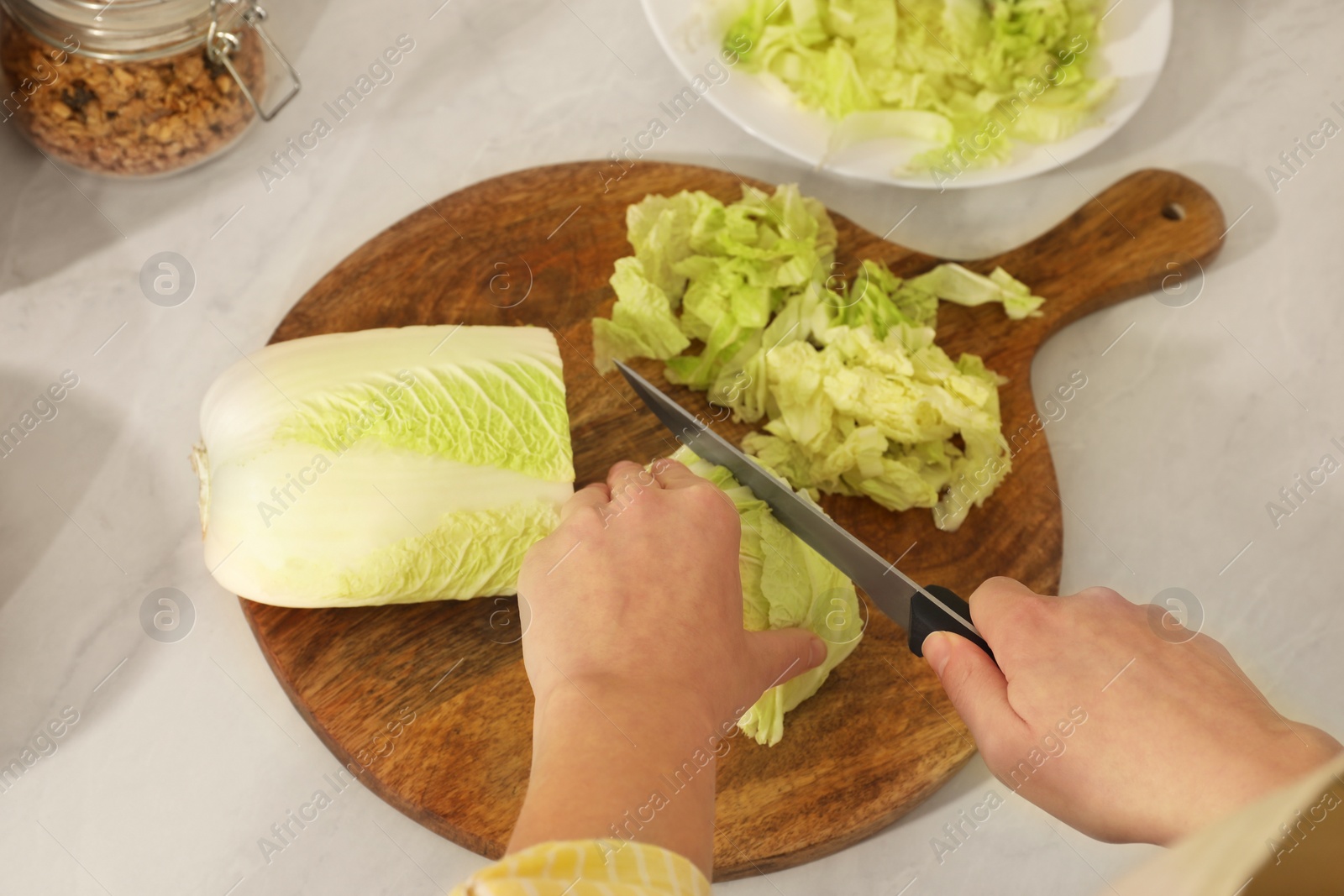 Photo of Woman cutting fresh chinese cabbage at kitchen table, closeup