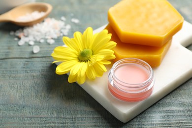 Photo of Lip balm, natural beeswax and flower on blue wooden table, closeup