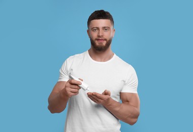 Photo of Handsome man applying body cream on light blue background