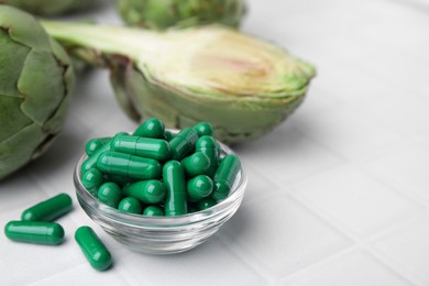 Photo of Bowl with pills and fresh artichokes on white tiled table, closeup. Space for text