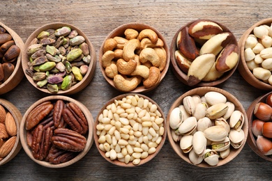 Photo of Flat lay composition with organic nuts on wooden background, top view. Snack mix