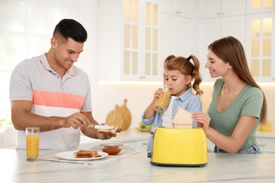 Happy family having breakfast with toasted bread at table in kitchen